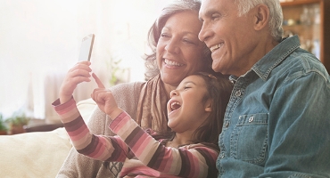 Grandparents with grandchild on their lap, all smiling. Child takes a selfie of group; represents Highmark Medicare Plans.