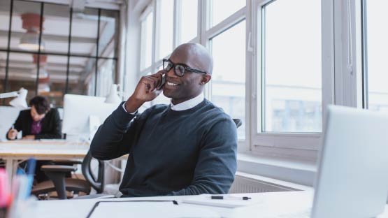 Smiling man sitting at desk on cell phone