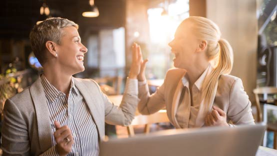 two smiling women high-fiving infront of an open laptop