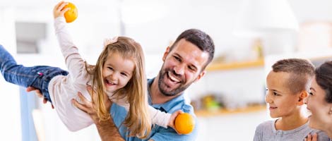 smiling father helicoptering his daughter while smiling son and mother look on