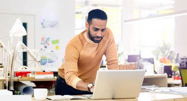 man standing at desk typing on a laptop