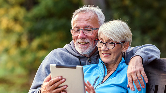 An older couple, a man and a woman, smiling and embracing outdoors.
