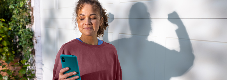 young female adult looking at her mobile device with her shadow behind her flexing her arm muscles