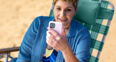 Smiling woman sitting on a chair outside looking at mobile phone to illustrate vast Highmark doctors network.