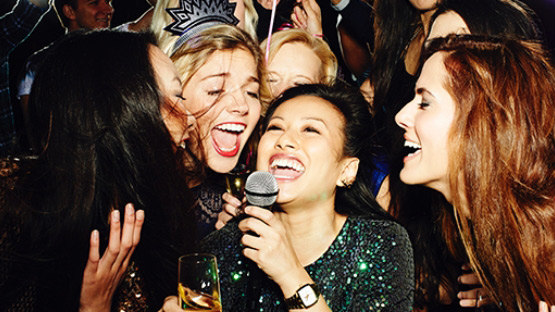 A group of happy women are singing karaoke together at a lively party, full of excitement and laughter.