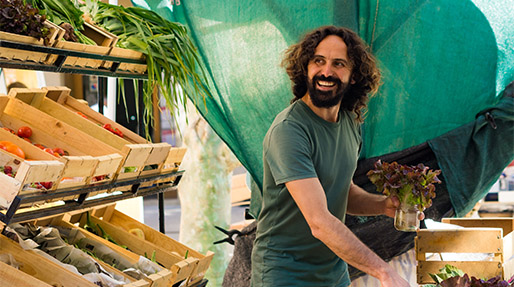 a man smiling selling vegetables at a farmers market