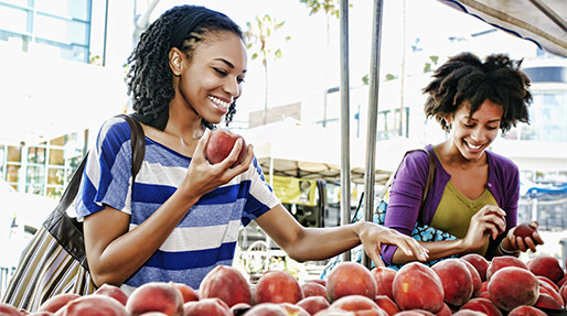 Two black women selecting peaches from a booth at a farmers market