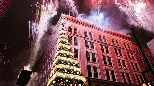 Penn Avenue Place building lit up with a Christmas tree on the corner and fireworks exploding in the sky above
