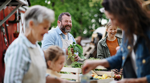 a man smiling holding vegetables while selling them and talking to visitors at a famer