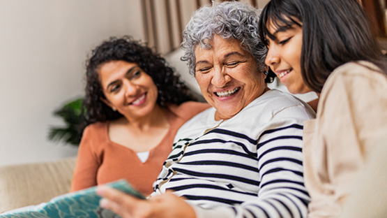 Three people are smiling and looking at something together on a couch.