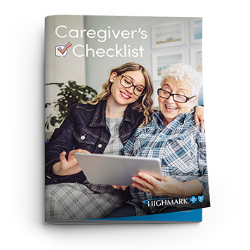 A younger woman and an older woman are looking at a tablet on a couch, with a Caregiver's Checklist booklet in the foreground..
