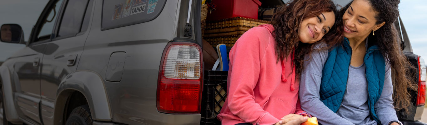 Two women sit close together in the back of a car, looking happy and relaxed together.