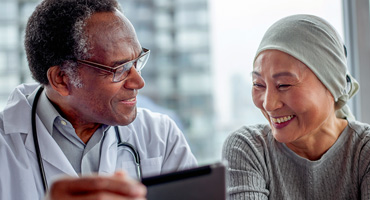 African American doctor and Asian patient wearing a light green scarf smiling.