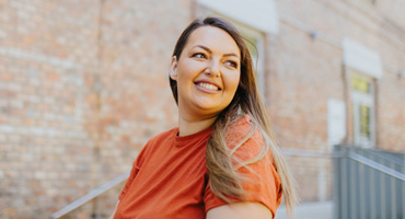 A woman smiling wearing an orange shirt and looking over her shoulder.