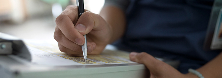 Closeup of person wearing a blue t-shirt filling out a form on a clipboard.