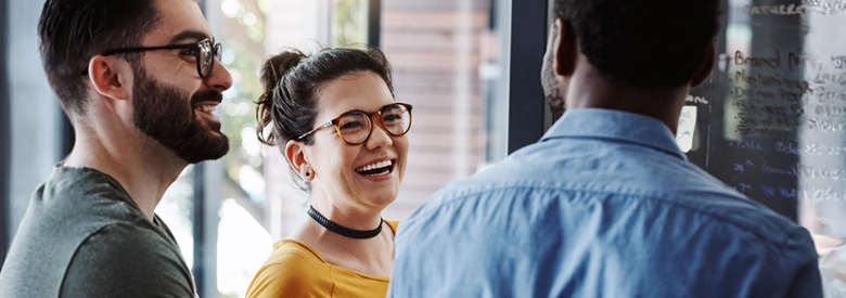 Three people work together in an office, as two smile and listen to the third person.