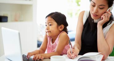 a little girl is on a laptop computer while the mother is busy working