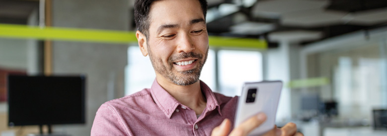 a happy adult, aged 30s-40s, smiles while looking at a cell phone in an office setting