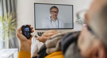 senior male on a video chat with a doctor while checking his blood pressure with a device