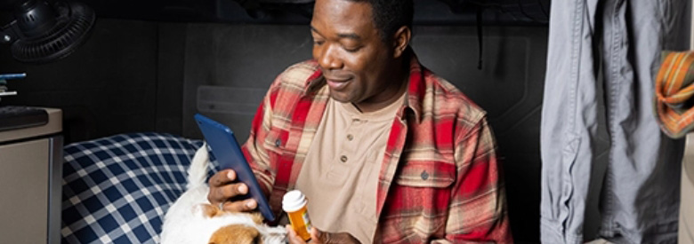 Black man sitting on his bed checking his Highmark health insurance prescription coverage on a tablet.