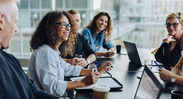 A diverse group of professionals smiling and collaborating around a conference table in a modern office.