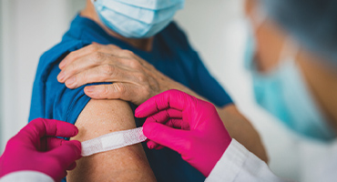 photo of a man receiving a covid-19 vaccine and then a bandage is being placed on his arm