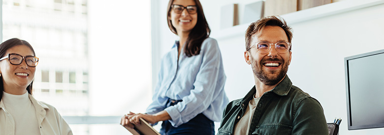 Two women and one man smiling colleagues in an office setting.