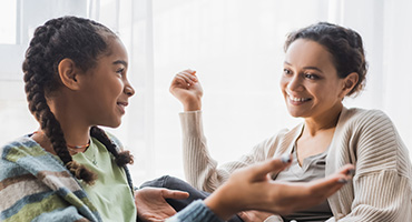 Two young adults talking. One has two braids and a green shirt.