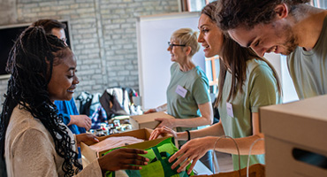 Group of smiling people wearing green shirts packing boxes