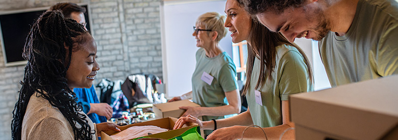 Group of smiling people wearing green shirts packing boxes