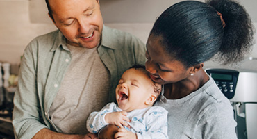 A joyful family, with a dad, a mom, and a baby who is laughing with their mouth wide open.