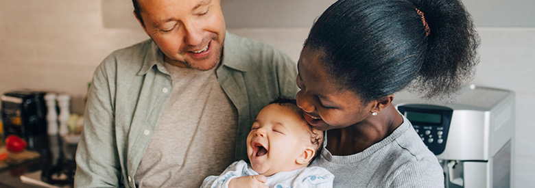 A joyful family, with a dad, a mom, and a baby who is laughing with their mouth wide open.