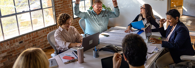 A diverse group of employees sitting around a conference room table, celebrating some behavioral health achievements.