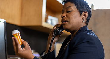 person inspecting a prescription bottle while on the phone