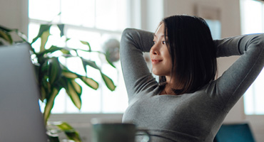 A woman working from home, sitting at a table with a laptop and coffee