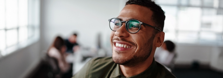 smiling man in an office setting with a table of coworkers in the background