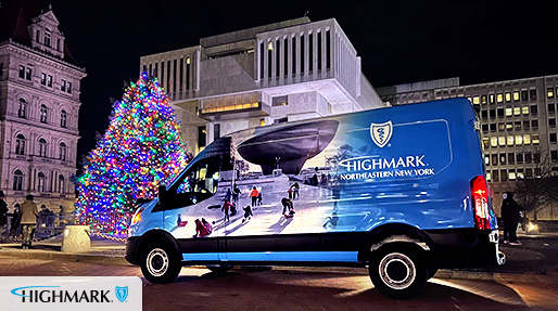 A Highmark Northeastern New York branded van, featuring an image of people ice skating with a sculpture in the background, is parked at night in front of a brightly lit Christmas tree and buildings. The Highmark logo is visible in the bottom left corner.