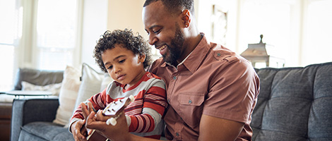 A dad and a young boy look at something on a tablet together.