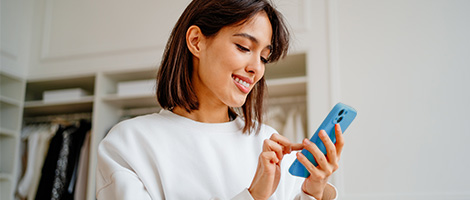 A woman smiles while looking at her phone.
