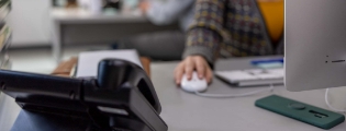 office scene showing a close up of a phone and a hand on a computer mouse