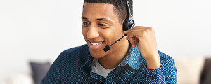 A smiling man with short dark hair, wearing a headset and a blue collared shirt, looking directly at the viewer. He appears ready to assist, representing customer service.