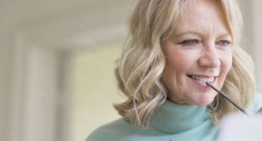 Smiling older woman with blond hair and light green turtleneck holds a pen to her face and considers Highmark Medicare Plans