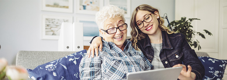 younger women embracing a senior women while looking at a digital tablet