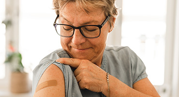 Woman with short hair and glasses, smiling at the Band-Aid on her arm; ready to learn about Highmark Medicare Plans and vaccines