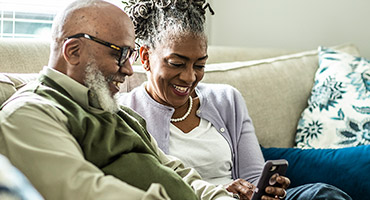 a senior couple sitting on a couch looking at a smart phone