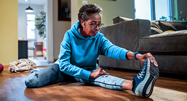 Fit older black woman on a hardwood floor near couch in workout clothes doing a stretch represents Highmark Medicare Plans