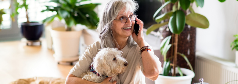 Retirment-age woman holding a dog and smiling while on the phone with a Medicare advisor.