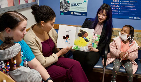 Three adults and two children, one adult is ready a book and showing pictures to the children