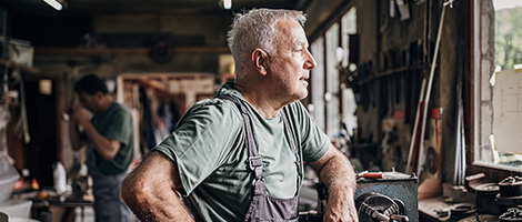 Older man on the job at a workshop looking out a window to the outdoors to to illustrate different types of depression.