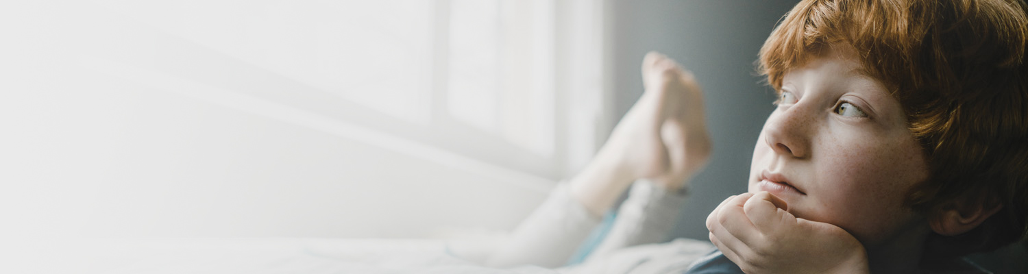 A young boy on his bed looking out the window to illustrate mental health for children and adolescents.